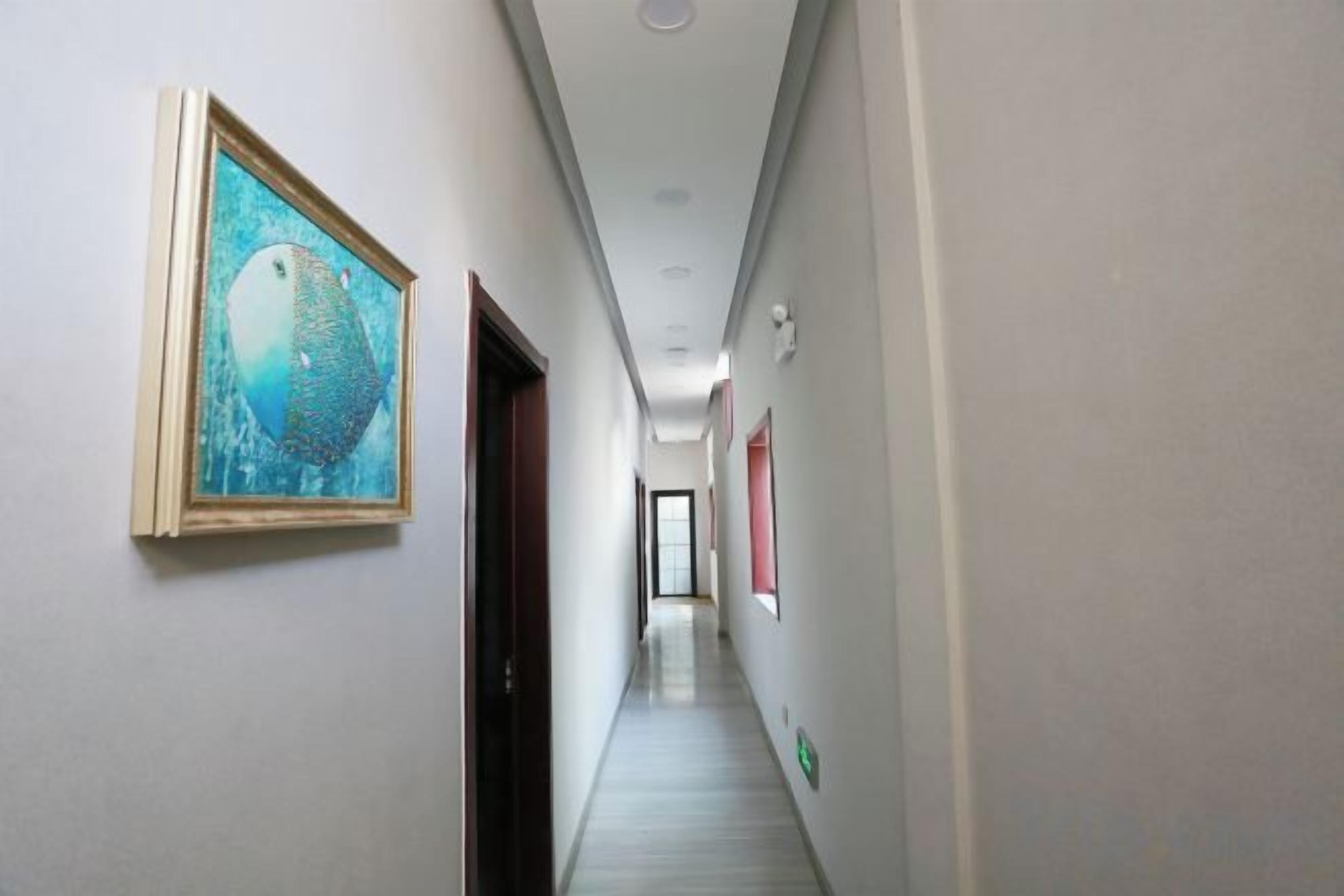 A corridor with a framed artwork on the left, a door on the right, and a hallway leading to a room.
