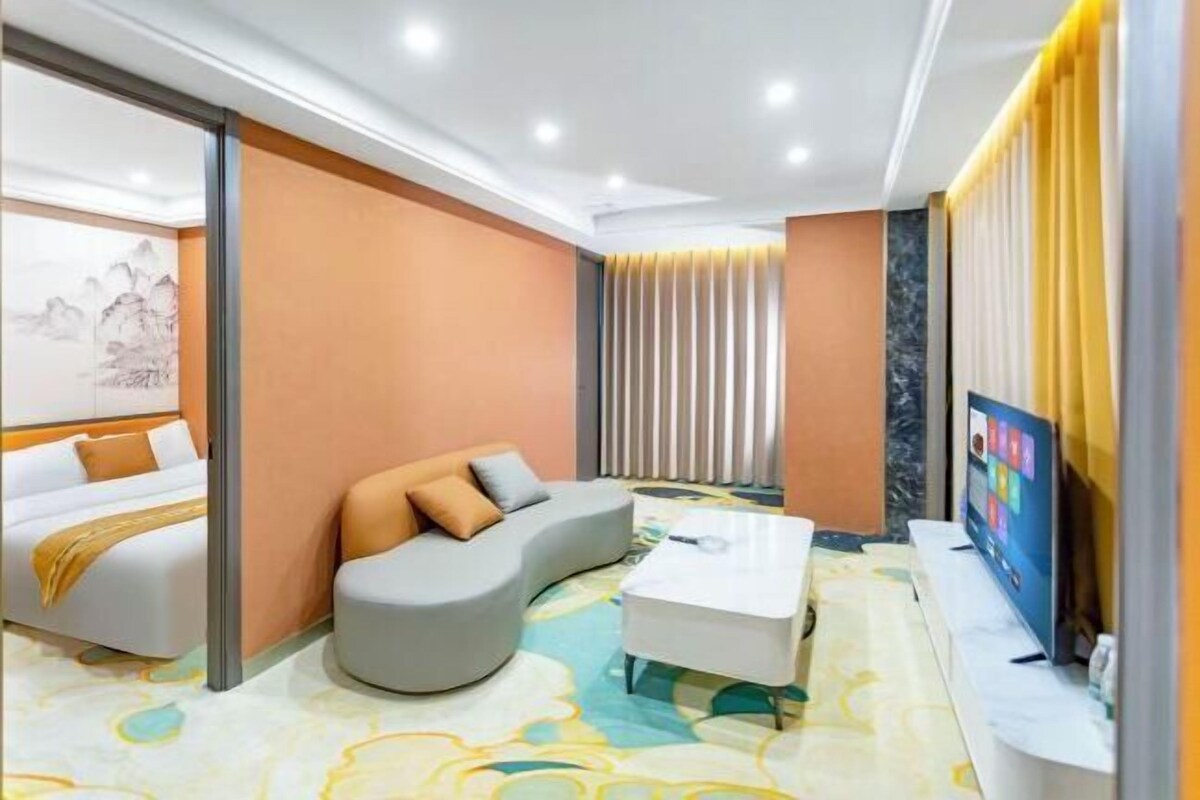 A modern hotel room with a bed, a curved gray sofa, a white coffee table, and a TV.
