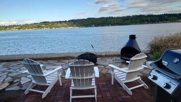 Une terrasse au bord de l’eau, dotée de fauteuils Adirondack et d’un barbecue Weber Spirit.
