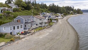 Une zone résidentielle côtière, avec des maisons construites le long d’une plage de sable, une vue dégagée sur l’eau et une colline boisée en arrière-plan.