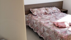 Un dormitorio con una cama cubierta con ropa de cama estampada, una mesita de noche y un pequeño calentador en el suelo.