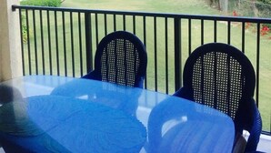 Un balcone con due sedie e un tavolo, affacciato su una spiaggia con palme e un cielo sereno.