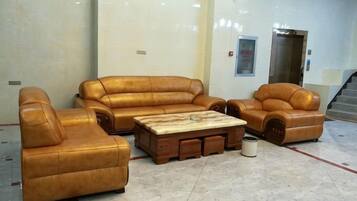 A lobby with a brown leather sofa set, a wooden coffee table, and a trash can.