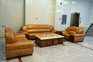 A lobby with a brown leather sofa set, a wooden coffee table, and a trash can. - Sun City Business Hotel (Yongren)
