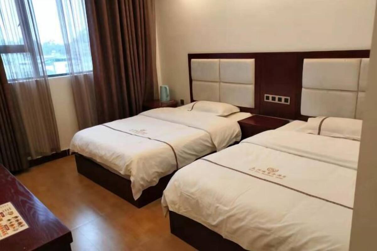 A hotel room with two beds, a wooden headboard, a nightstand, and a window with curtains.