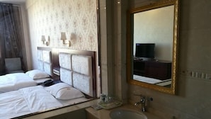 A hotel room with two beds, a large mirror, a sink, and a television in the corner.