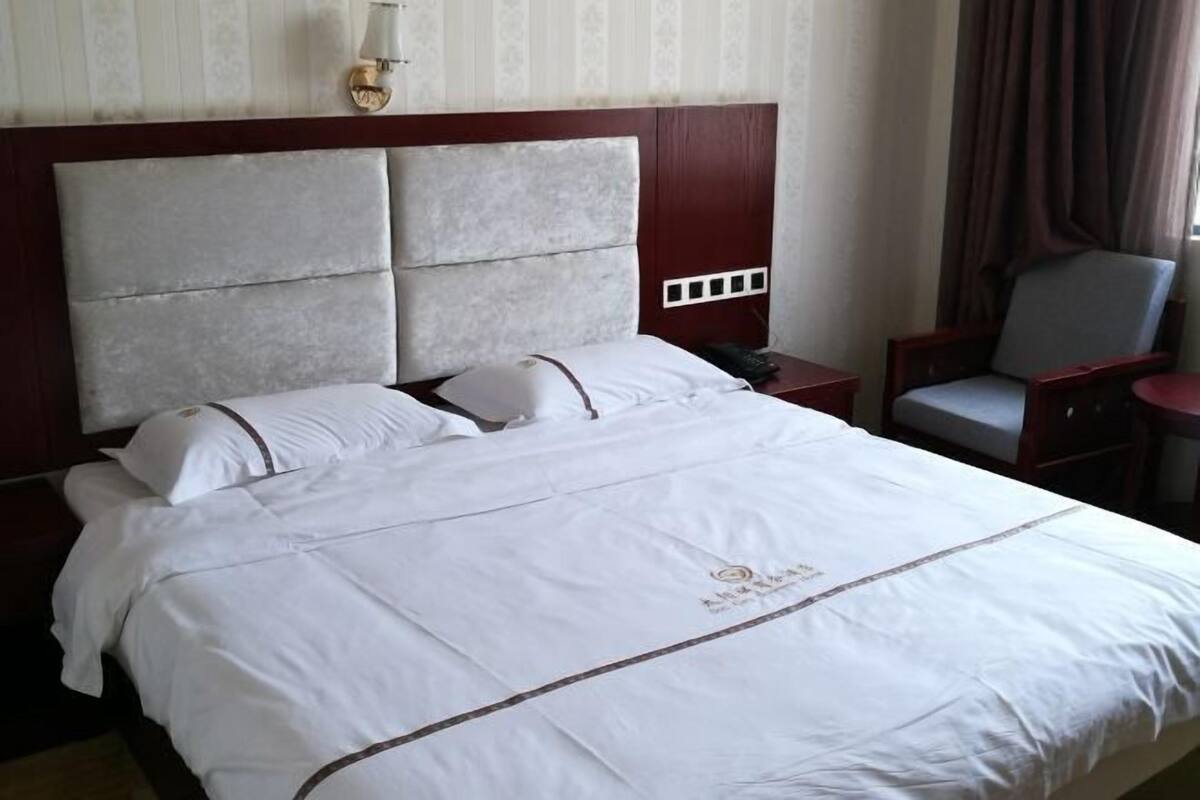 A hotel room with a large bed, a nightstand, a chair, and a wall-mounted lamp.