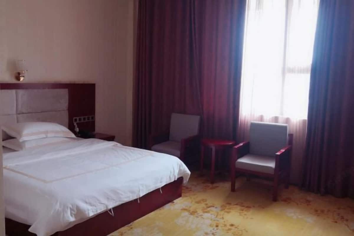 A hotel room with a bed, a chair, a small table, and a window with curtains.