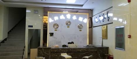 A reception area with a marble counter, three bar stools, a staircase, and a framed picture on the wall.