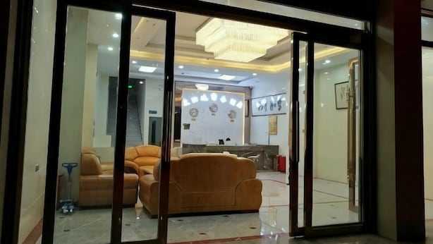 A hotel lobby with a reception desk, seating area, and a chandelier.