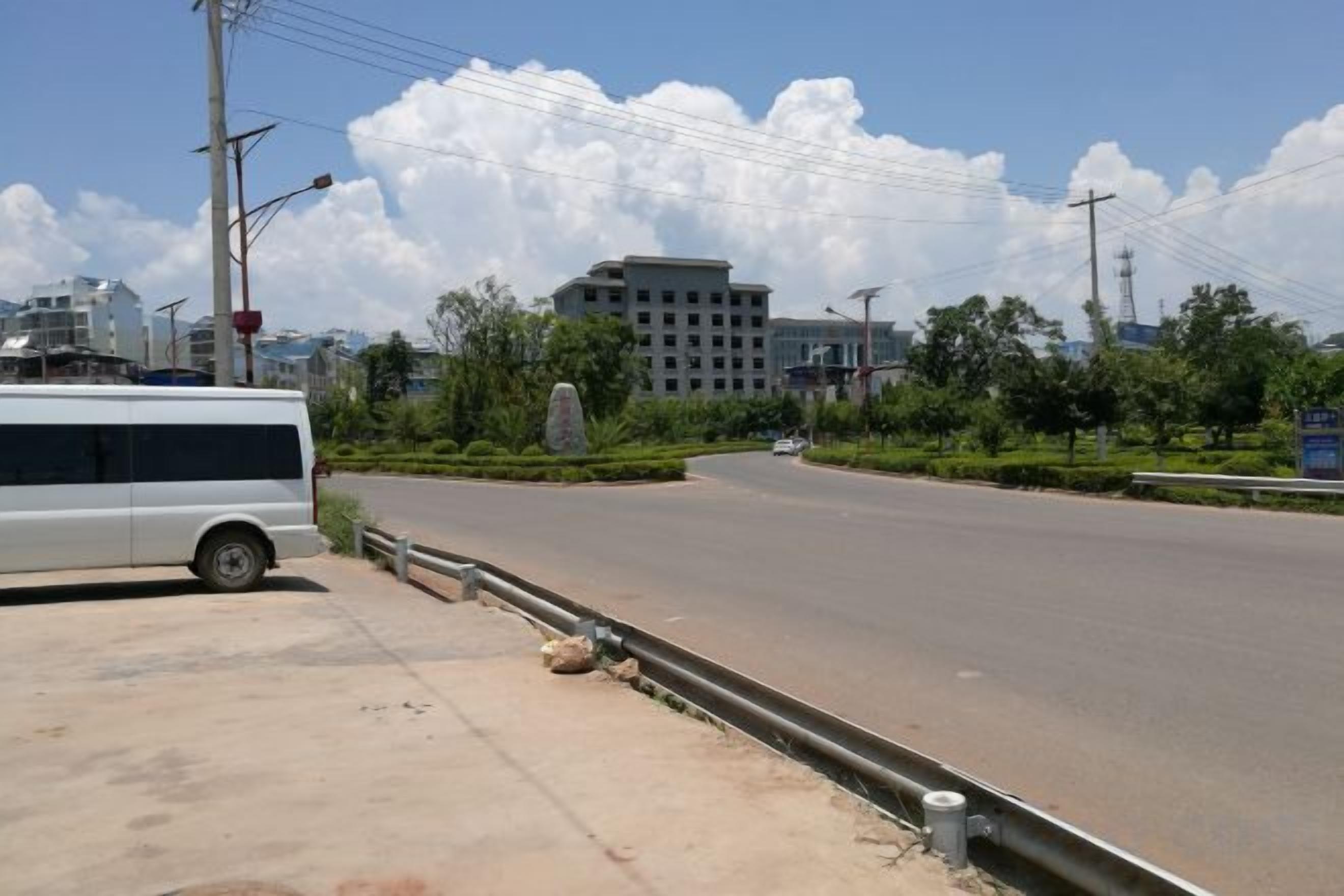 A road with a white van parked on the side, a clear sky, and buildings in the background.