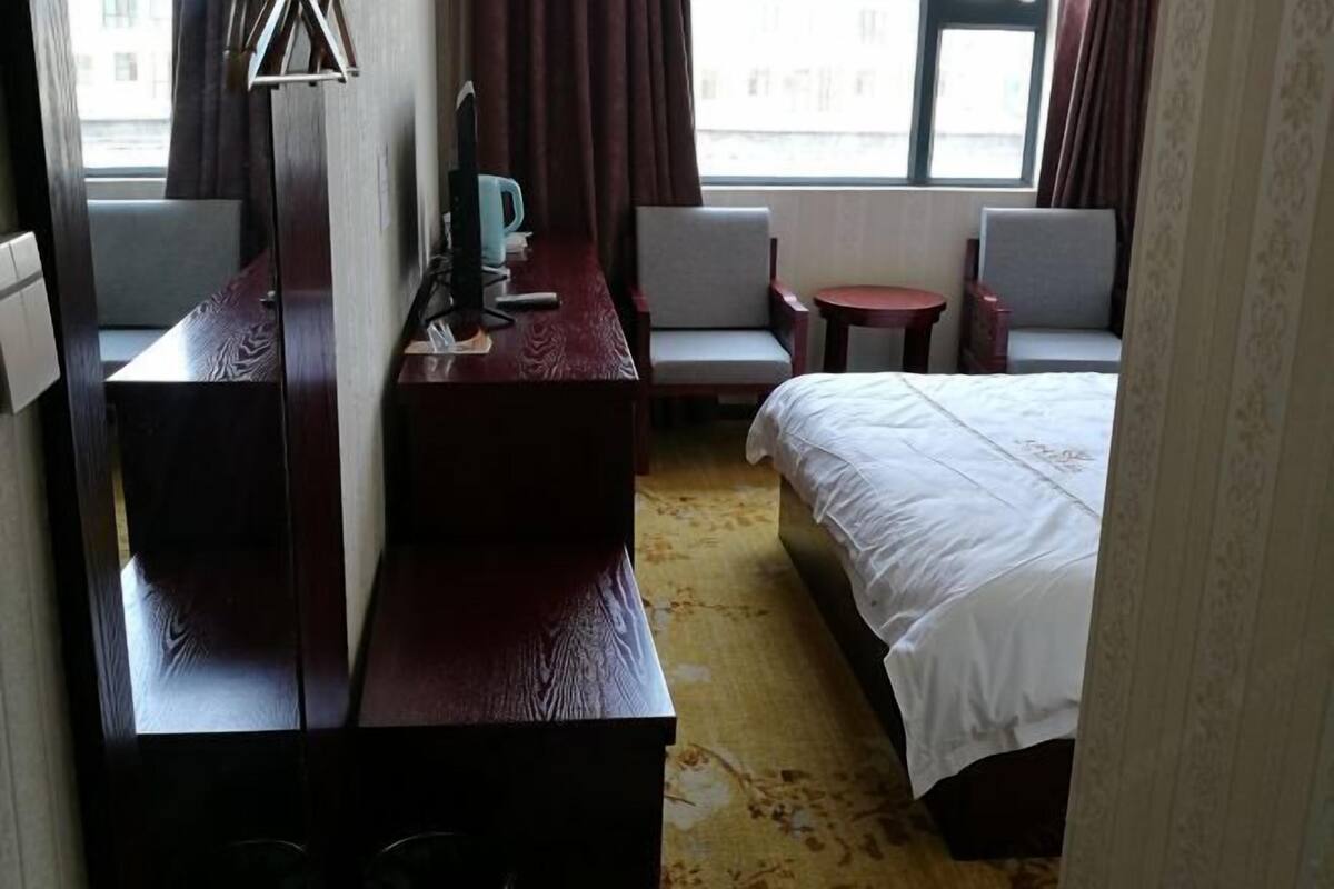 A hotel room with a bed, a desk, two chairs, a small table, and a window with curtains.