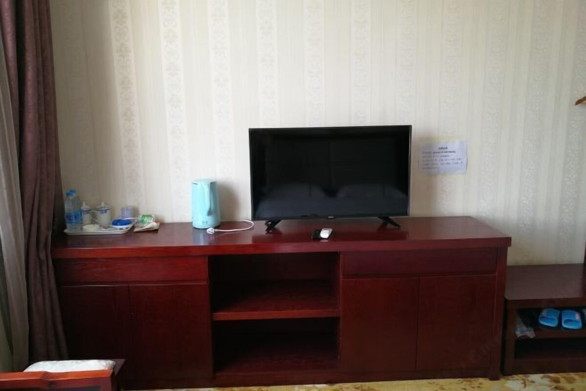 A room with a wooden desk, a television, and a small shelf with slippers.