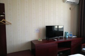A hotel room with a TV on a wooden dresser, a small table with a kettle and water bottles, and a hanging coat rack. - Sun City Business Hotel (Yongren)