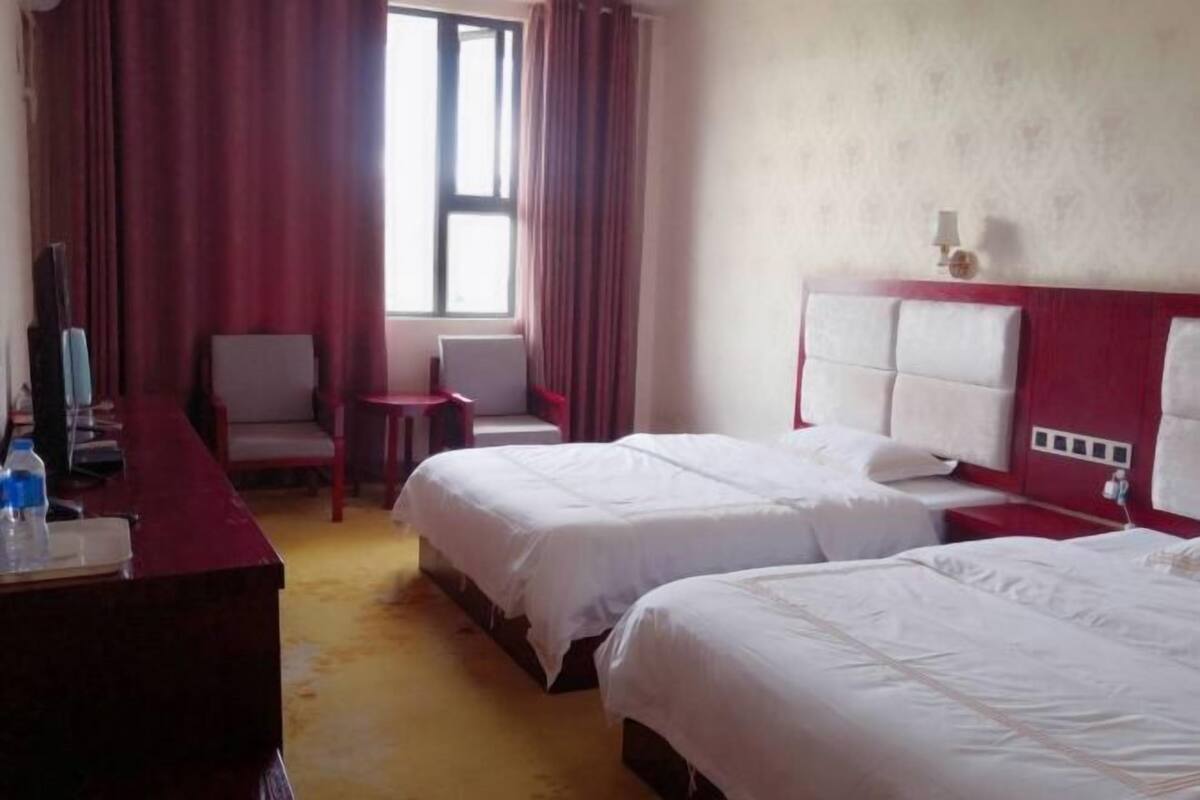 A hotel room with two beds, a desk with a chair, a small table, and a window with curtains.