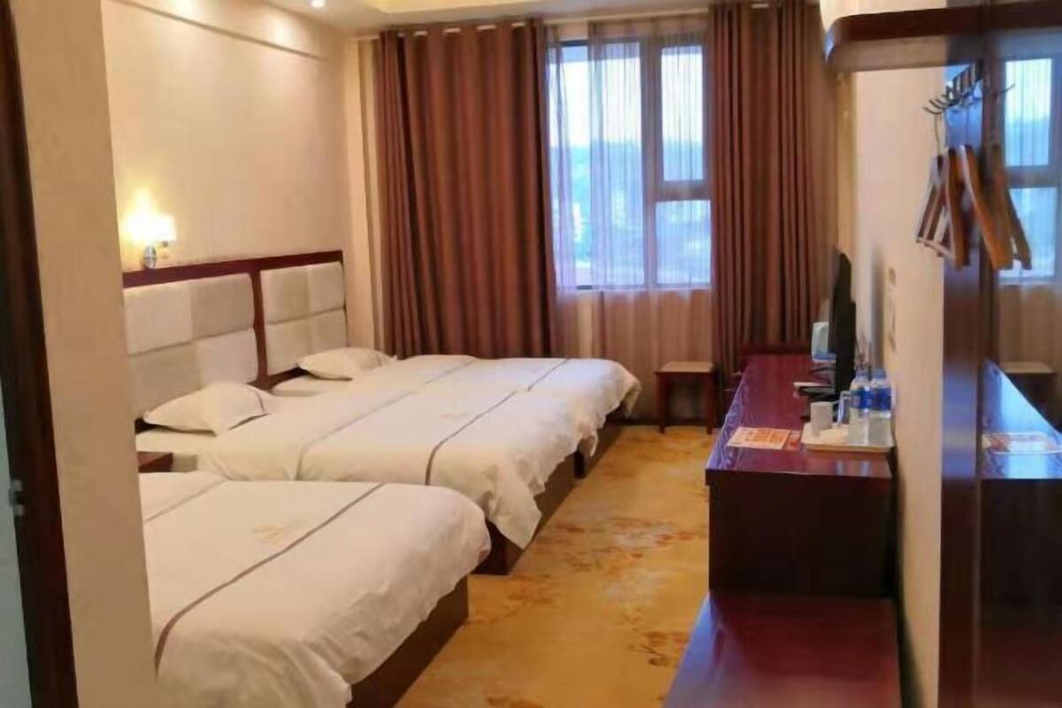 A hotel room with two beds, a desk, a chair, and a window with curtains.