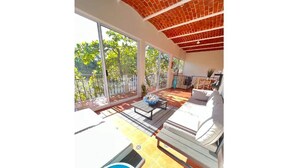 Un balcón amplio con piscina, mobiliario exterior y ventanas grandes que ofrecen vistas a árboles.