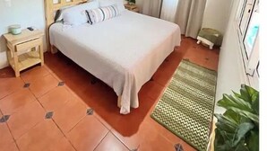 Un dormitorio con techo de ladrillo, una cama con cabecera de madera, una mesita de noche, un televisor montado en la pared y una planta en maceta.