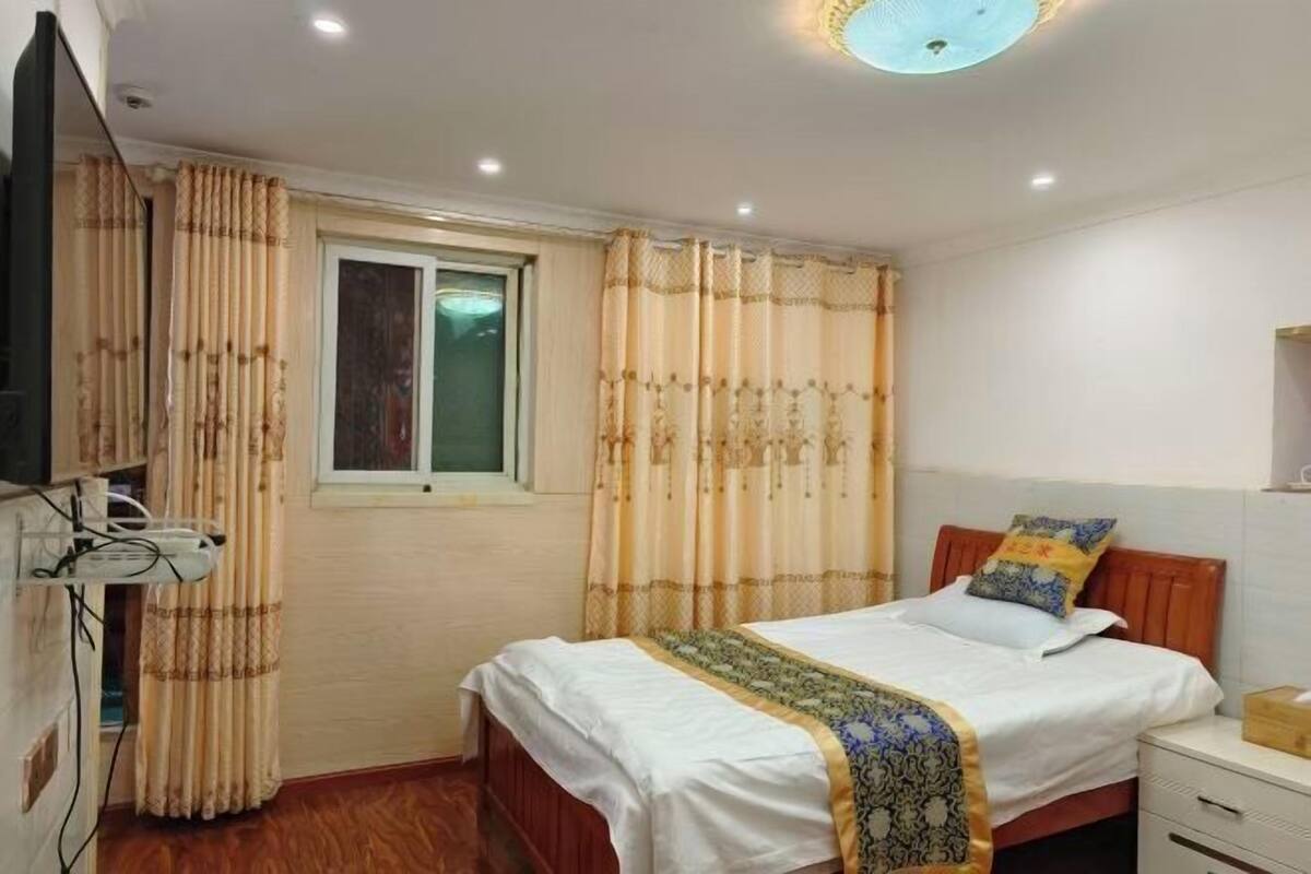 A bedroom with a bed, curtains, a window, a bedside table, and a television.