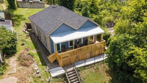 A two-story house with a balcony and a small deck, surrounded by trees and a paved driveway.