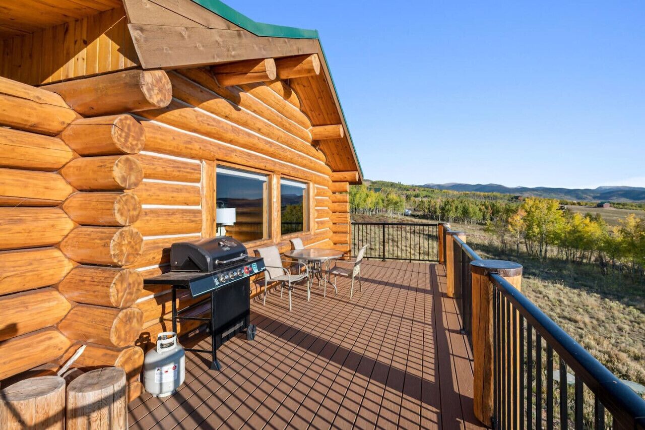 A log cabin with a deck, a grill, and outdoor seating.