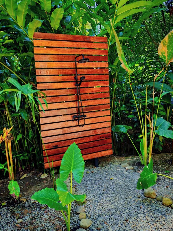 A wooden bench with a black metal structure attached to it, surrounded by lush green foliage and pebbles. - Green Jungle House (Cahuita)