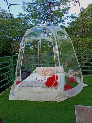 Ein durchsichtiges Himmelbett mit weißer Matratze, Kissen und roten Dekorationselementen.