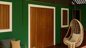 Una habitación con pared verde, suelo de madera, una silla de mimbre, un sofá y una puerta de madera.