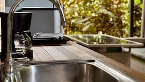Una cocina con un lavamanos de acero inoxidable, una cafetera y una ventana con vista a un jardín exuberante.