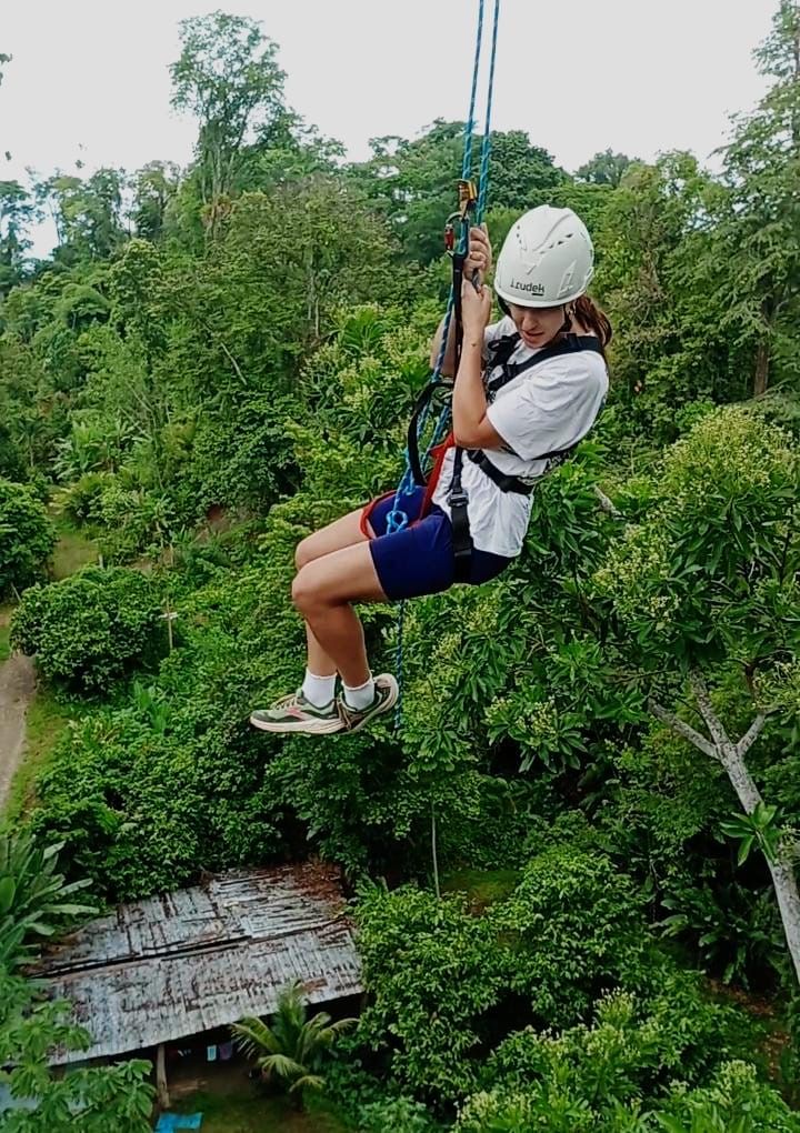 Una persona deslizándose en tirolesa por un bosque verde y frondoso.