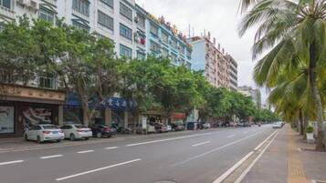 A street lined with multi-story buildings, parked cars, and palm trees.