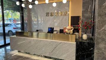 A hotel reception desk with a marble counter, a digital screen, and a vase with flowers.