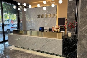 Una recepción de hotel con mostrador de mármol, una pantalla digital y un jarrón con flores.