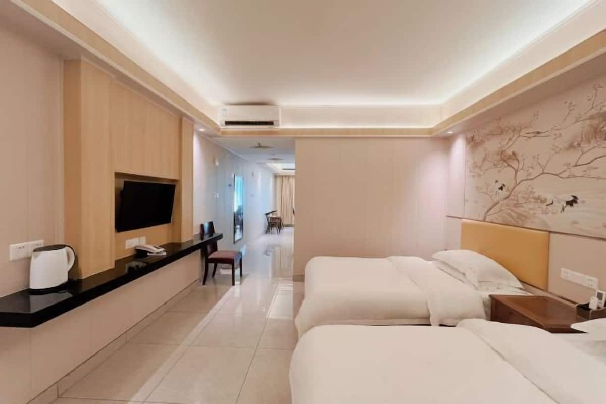 A hotel room with a bed, a desk with a telephone, a television, and a wall-mounted air conditioner.