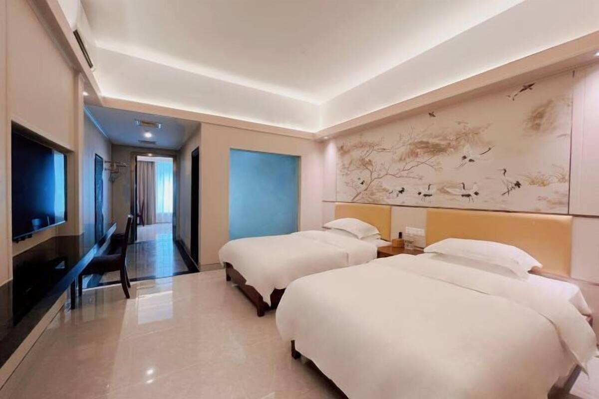 A hotel room with two beds, a TV, a large wall mural, and a hallway leading to another room.