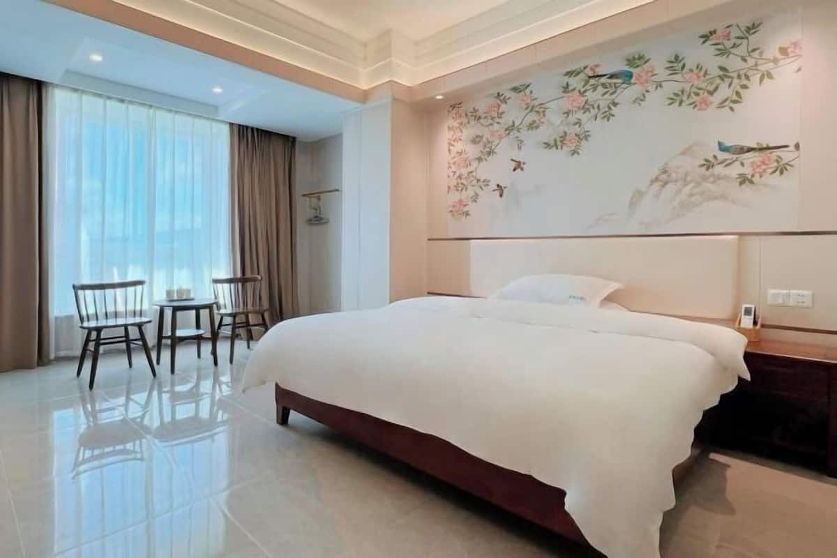 A hotel room with a large bed, a dining area with chairs, a wall with a floral mural, and a large window with curtains.