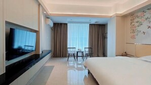 Quarto de hotel com cama, televisão, mesa pequena com cadeiras e janela com cortinas.