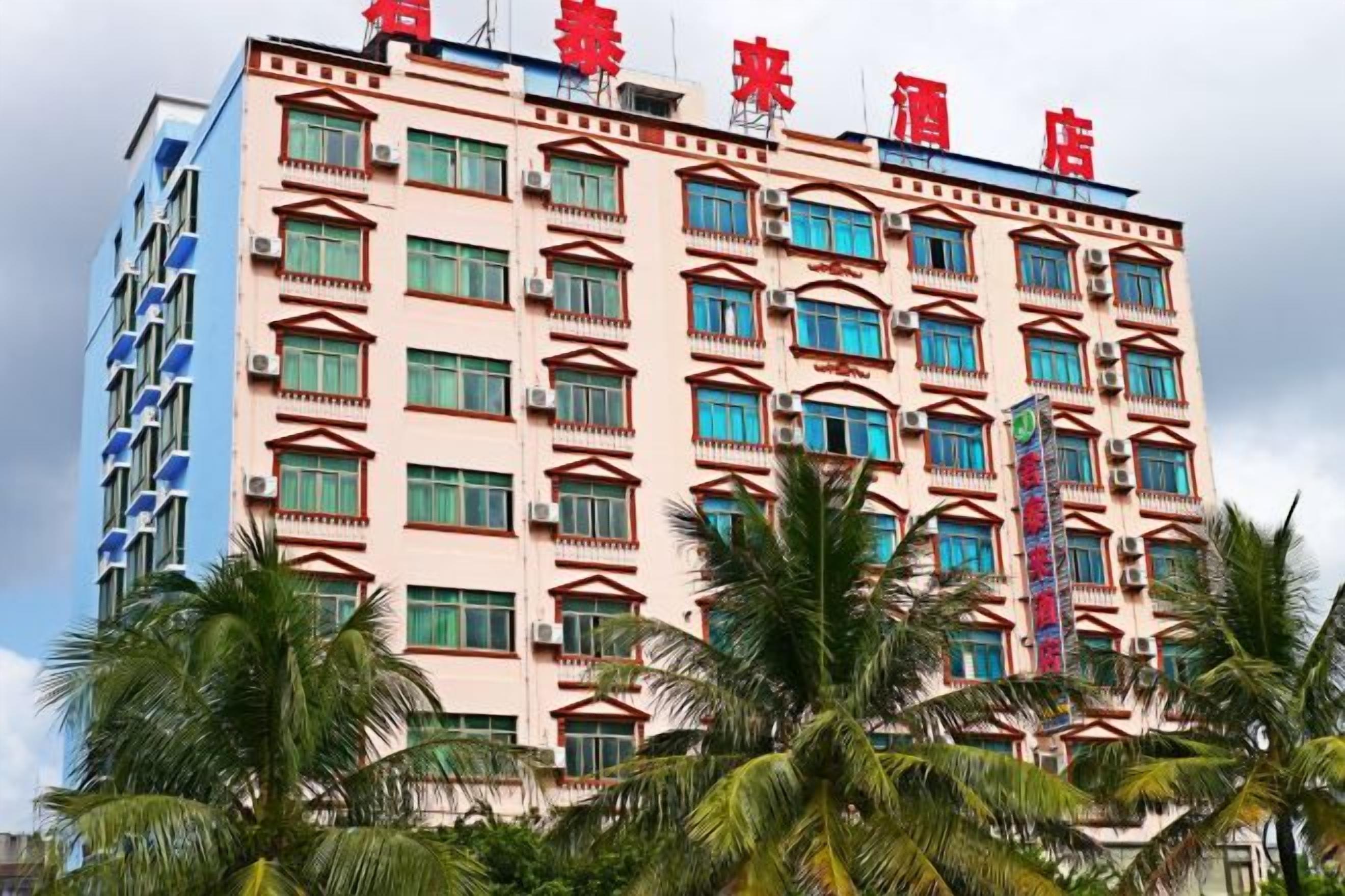 A multi-story hotel with a red sign on the top, balconies on the upper floors, and palm trees in the foreground.