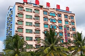 A multi-story hotel with a red sign on the top, balconies on the upper floors, and palm trees in the foreground. - Juntailai Hotel (Wenchang)