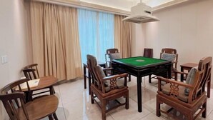 Quarto com mesa de bilhar, cadeiras de madeira, uma pequena mesa com cadeira e janela com cortinas.