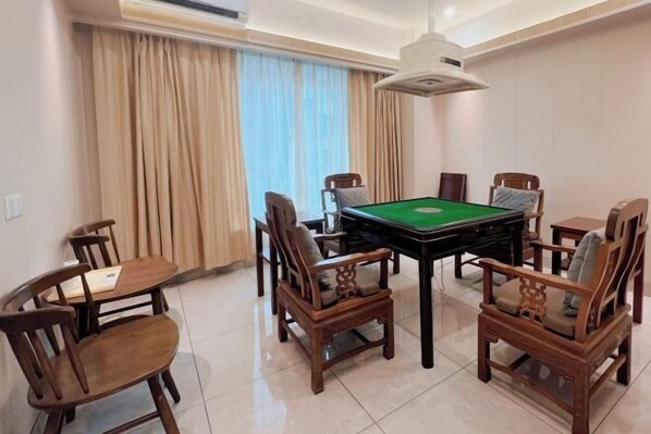 A room with a pool table, wooden chairs, a small table with a chair, and a window with curtains. - Juntailai Hotel (Wenchang)