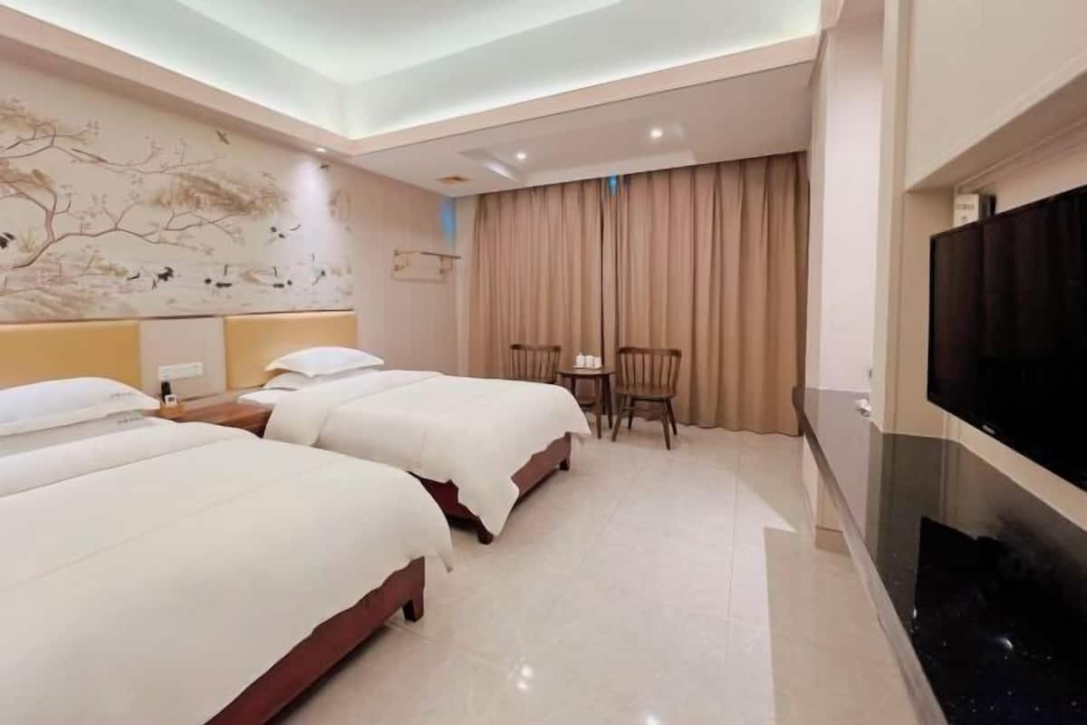 A hotel room with two beds, a television, a desk, and a chair.