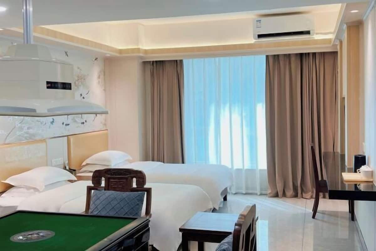 A hotel room with two beds, a pool table, a desk, and a large window with curtains.