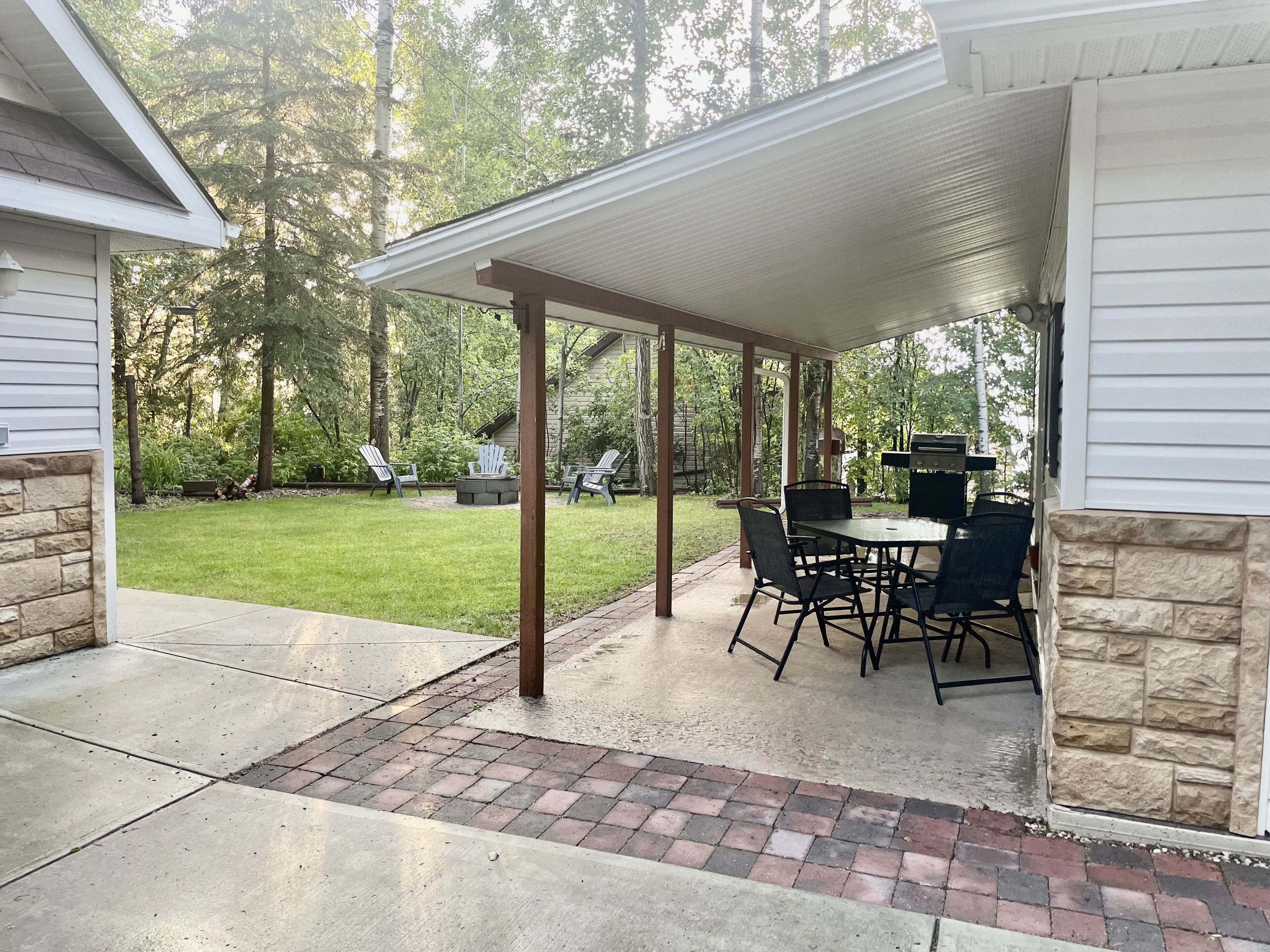 A covered patio area with a table and chairs, a grill, and a fire pit.