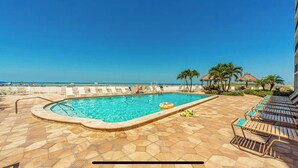 A swimming pool with lounge chairs and palm trees, overlooking a beach. - Modern Oceanview Heated pool overlooking Mad Beach (Madeira Beach)