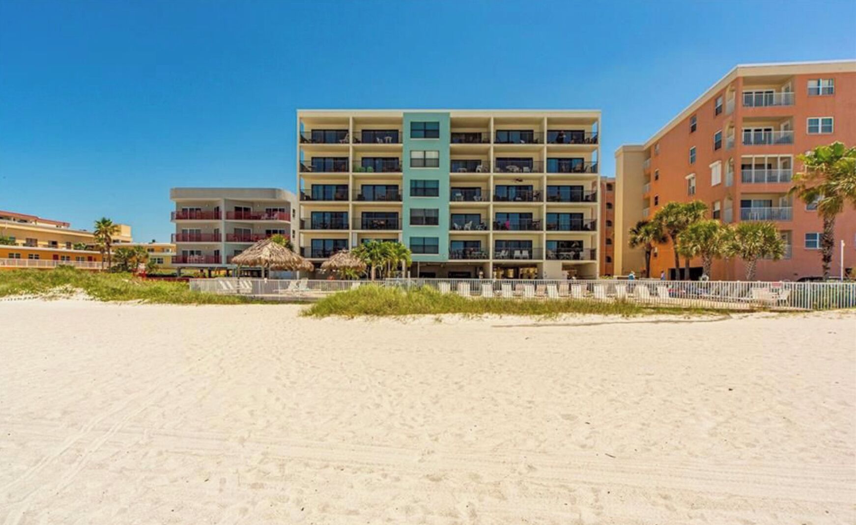 Hotel aan het strand met meerdere verdiepingen, een zandstrand op de voorgrond en palmbomen.