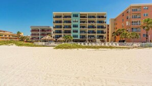 A beachfront hotel with multiple floors, a sandy beach in the foreground, and palm trees. - Modern Oceanview Heated pool overlooking Mad Beach (Madeira Beach)