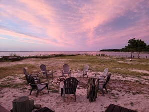 Ein Strandambiente mit Adirondack-Stühlen, die um eine Feuerstelle angeordnet sind.