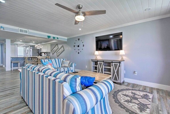 A modern living room with a striped sofa set, a wooden coffee table, a ceiling fan, and a TV mounted on the wall. - Beachfront Edgewater - 10th floor, private balcony, upgraded throughout (Panama City Beach)