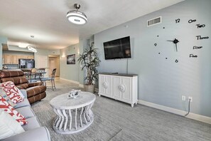 A modern living room with a sofa, a round coffee table, a TV mounted on the wall, and a decorative clock.